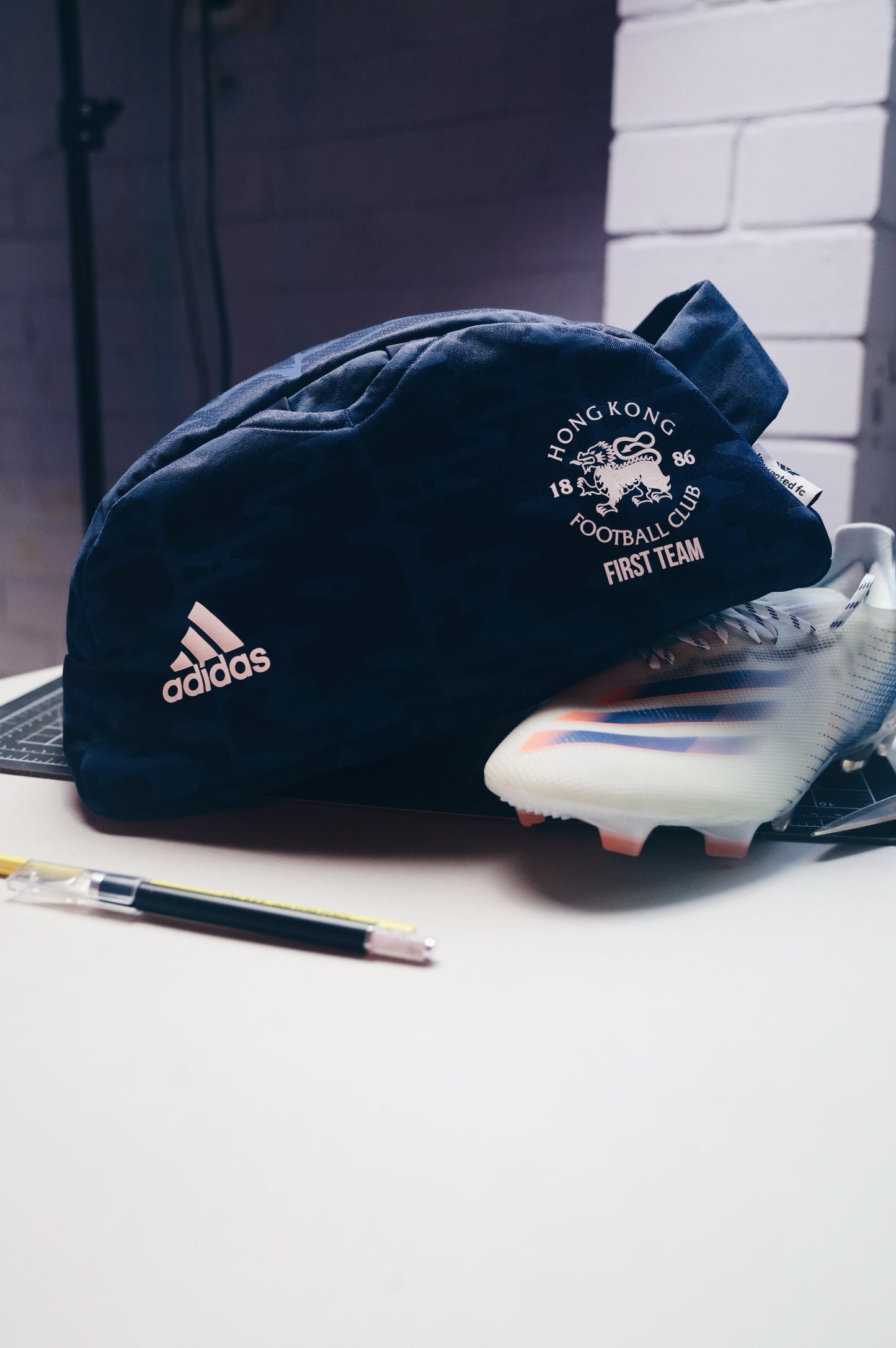 Navy blue cap with Adidas logo and Hong Kong Football Club First Team logo on a white surface.
