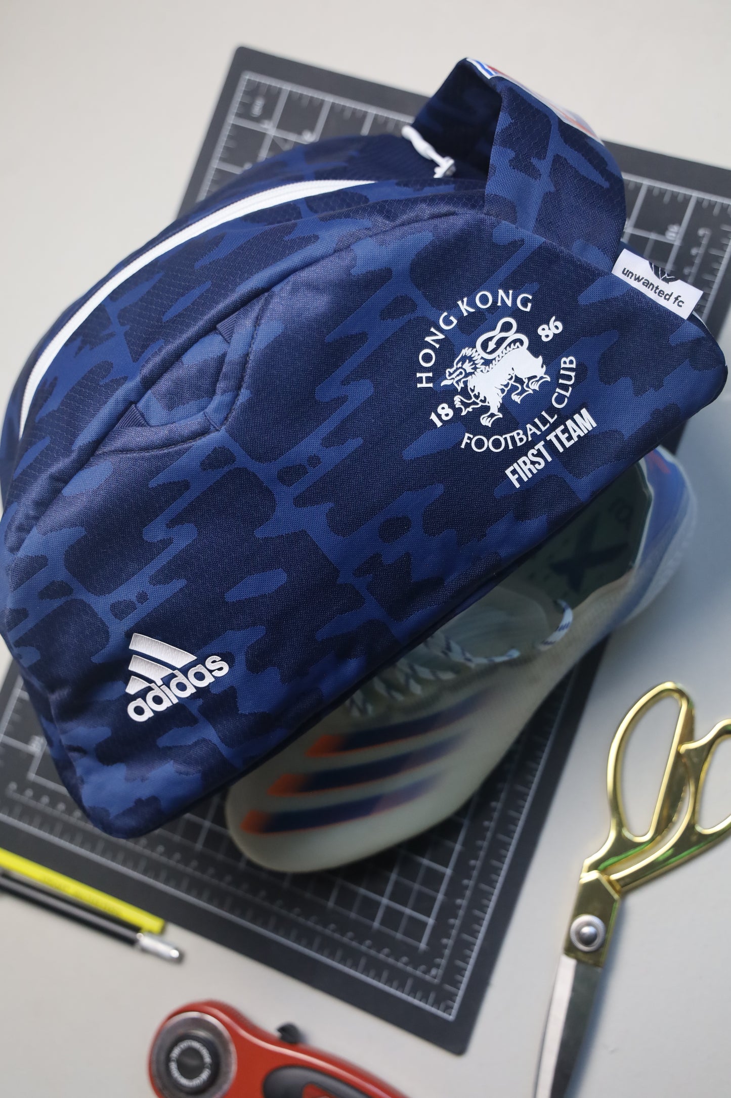 Blue Adidas bag with Hong Kong Football Club logo on a cutting mat with scissors and other items.